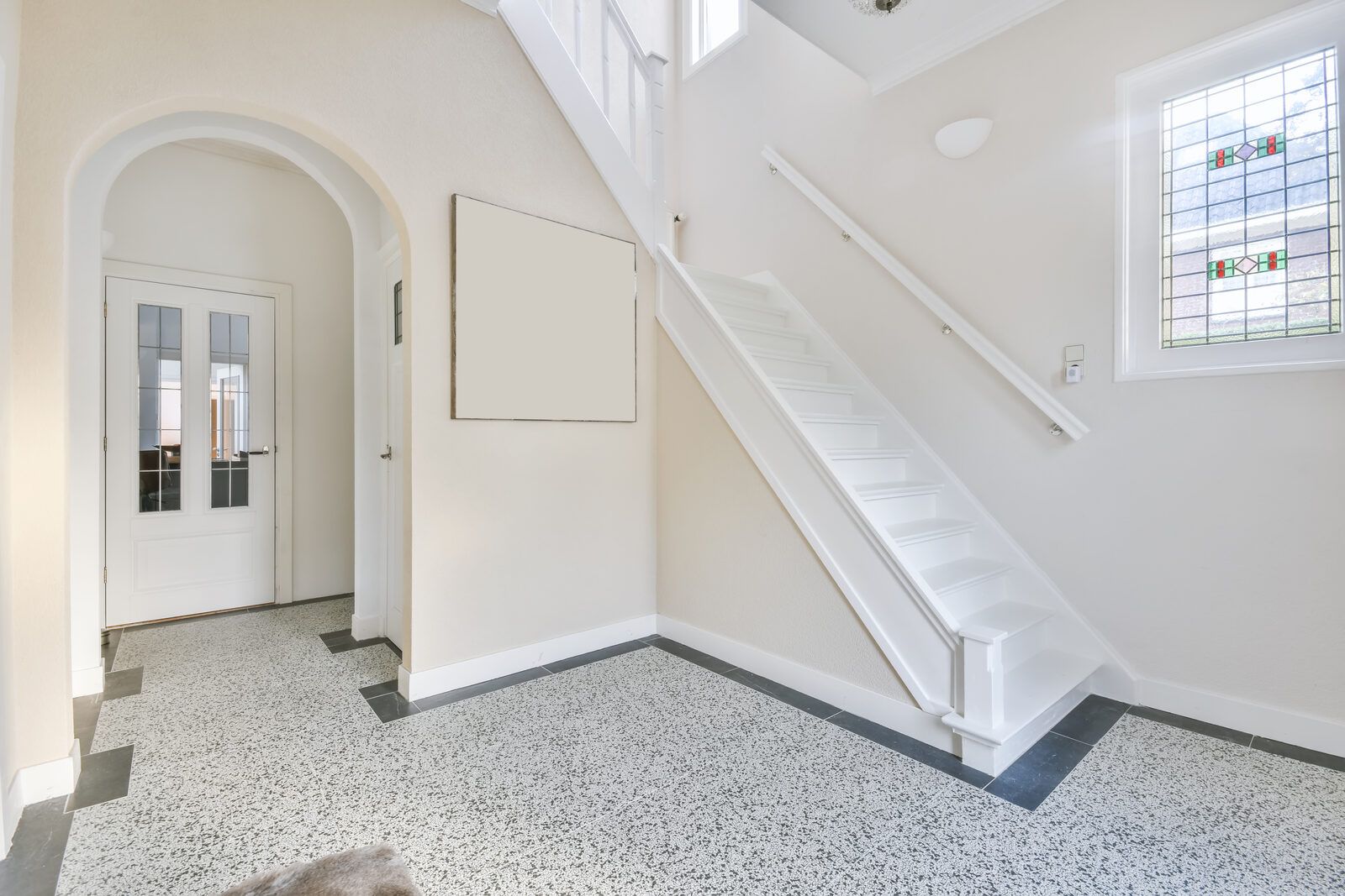Bright foyer with a light flake floor and white staircase